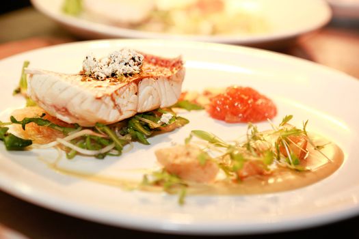 Delicious gourmet seafood meal with a grilled fish fillet served on fresh sliced vegetables and salad at a restaurant