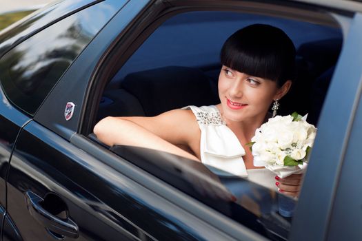 happy bride with flower bouquet siting in the car