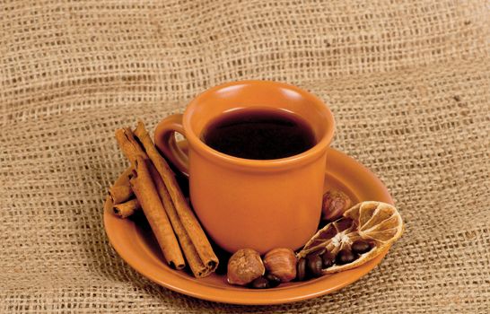Closeup shot of freshly prepared cup of italian espresso with cinnamon, coffe beans, nuts and lemon over sacking