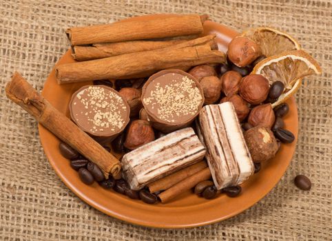 Sweets, cinnamon, nuts and coffee beans on a saucer, on burlap background.
