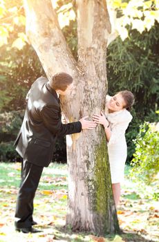 Young couple playing hide and seek around a tree