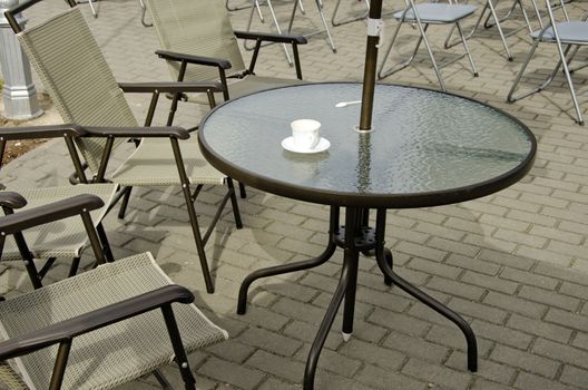 Empty coffee cup on table and chairs on pavement. Outdoor cafe.