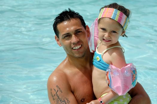 Father and daughter in pool. The facher is holding his daughter, they are smiling and looking.
