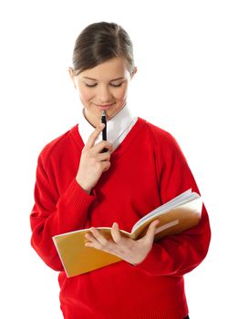 Girl thinking and looking into her notebook. Holding pen against her chin