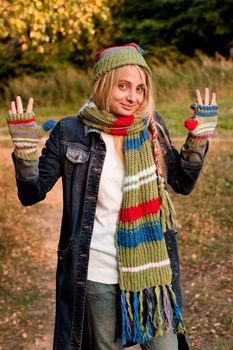 A standing girl in a cup and scarf and mittens and jeans coat in a forest
