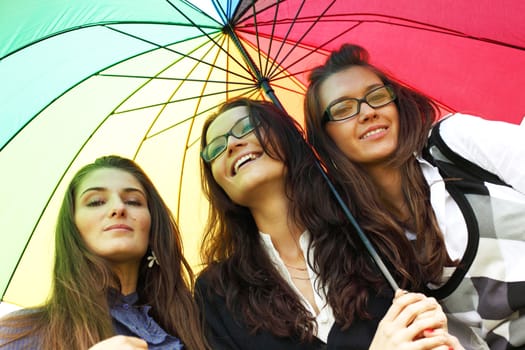 happy smiling girlfriends stay under colourful umbrella  