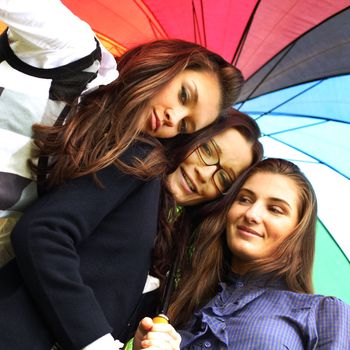 happy smiling girlfriends stay under colourful umbrella  