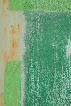 An old surface with worn layers of green paint with streaks of rust forming a variety of patterns and textures.