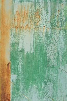 An old surface with worn layers of green paint with streaks of rust forming a variety of patterns and textures.