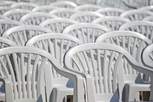 View of some white plastic cafe, restaurant or garden chairs, in an aligned fashion on a outdoor setting.