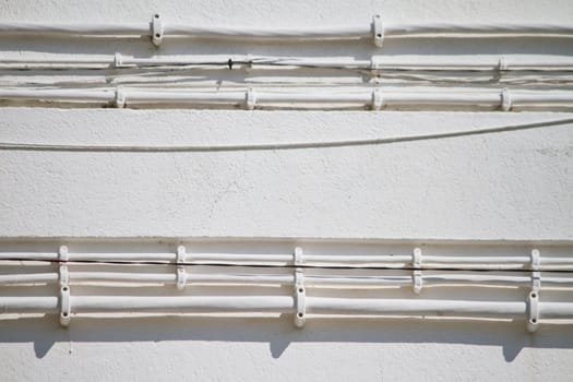 Close view of some old electricity cables attached to a white wall.
