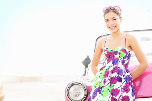 Car woman smiling happy standing in front of pink retro vintage car. Portrait of pretty girl in summer dress.  Multicultural Chinese Asian / Caucasian female lifestyle model. Photo from Havana, Cuba.