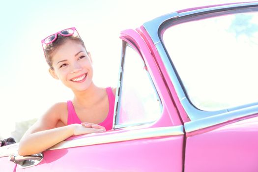 Woman driving vintage car. Retro style image of happy smiling young woman in old pink car going on road trip on sunny spring or summer day. Beautiful multiracial Caucasian / Chinese Asian lifestyle model outdoor. Photo from Havana, Cuba.