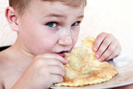 Closeup portrait of little boy eating meat pie named �cheburek�