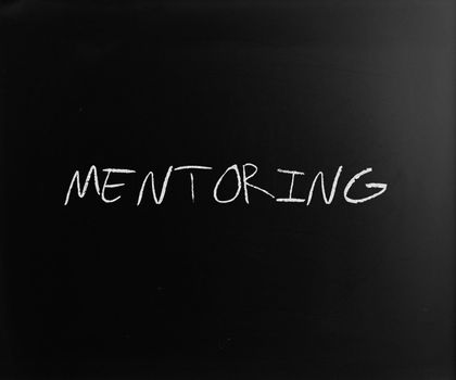 The word "Mentoring" handwritten with white chalk on a blackboard.