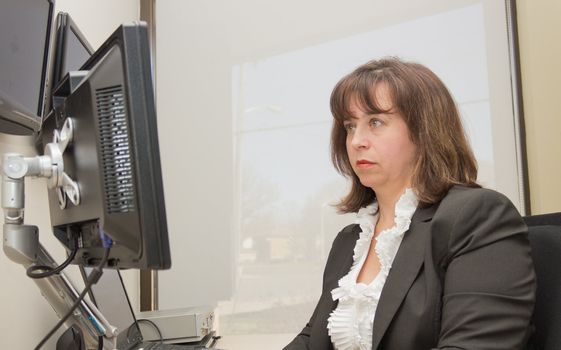 Business woman seated at desk looking at monitor