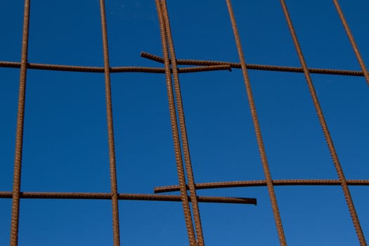 Metal, rusty steel, forms a grid, cage, against a clear blue sky.