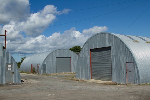 An industrial units made from corrugated metal sheets with a roller shutters and doors on rough ground.