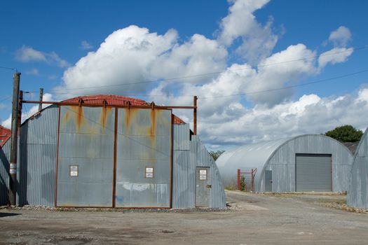 An industrial unit made from corrugated metal sheets with a sliding shutter and door on rough ground.