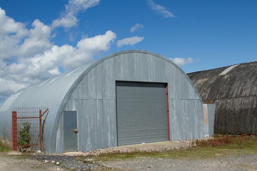 An industrial unit made from corrugated metal sheets with a roller shutter and door on rough ground.