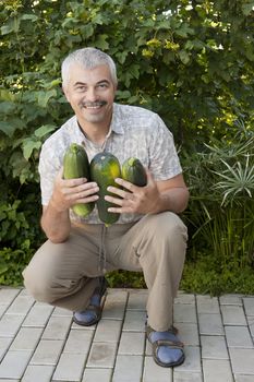 Satisfied man with three zucchini in garden