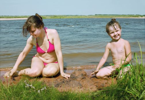 Mum with a daughter play on river bank in the afternoon