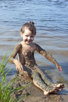 Naughty baby girl in the mud on the river
