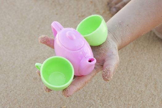 Toy cups in baby hand on the beach