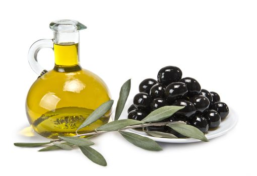 A jar with olive oil ans a plate with black olives on a wooden surface.