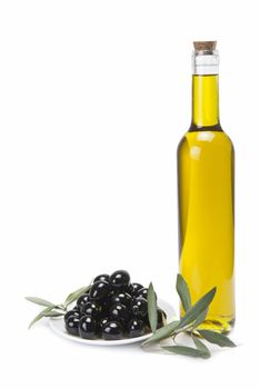 A classical glass bottle of olive oil and a plate with black olives isolated over a white background.