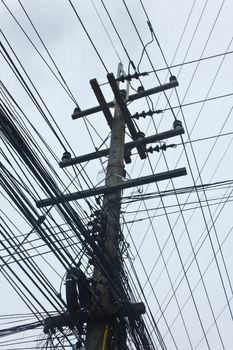 Stock Photo - messy old electricity post by the road with power line cables, transformers and phone lines (blue sky background)