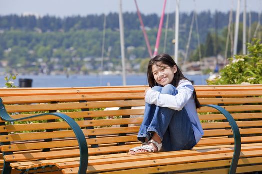 Happy ten year old girl enjoying the sun on bench by the lake