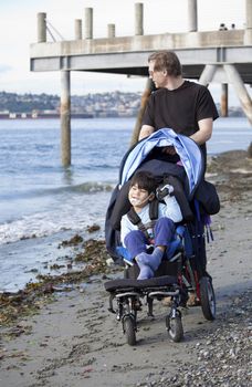 Father pushing wheelchair with disabled son on beach