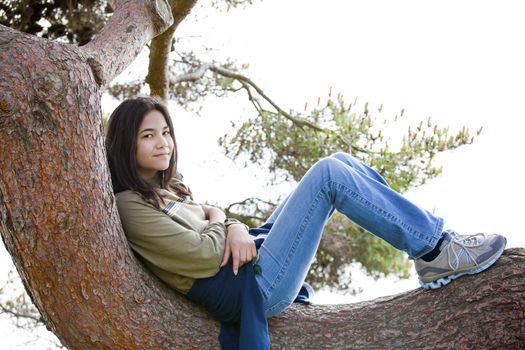 Young teen girl sitting on tree limb, relaxing