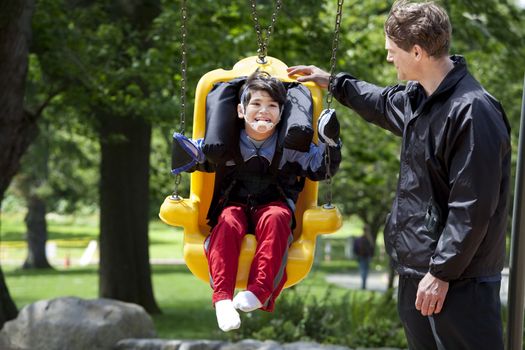 Father pushing disabled boy in special needs handicap swing. Child has cerebral palsy.