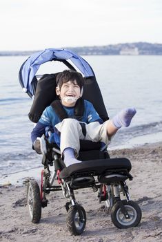 Happy disabled five year old boy in wheelchair on the beach