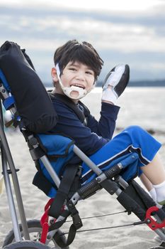 Happy disabled five year old boy in wheelchair on the beach, waving hello