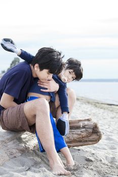 Big brother holding disabled boy on beach, helping  him play in the sand