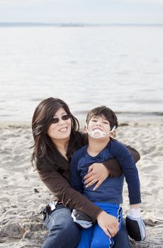 Mother holding her disabled son on the beach. Child has cerebral palsy