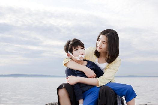 Teenage sister holding her disabled brother on the beach. Child has cerebral palsy