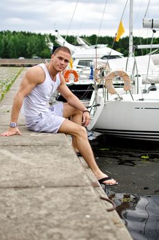 Attractive muscular male sitting near the yacht