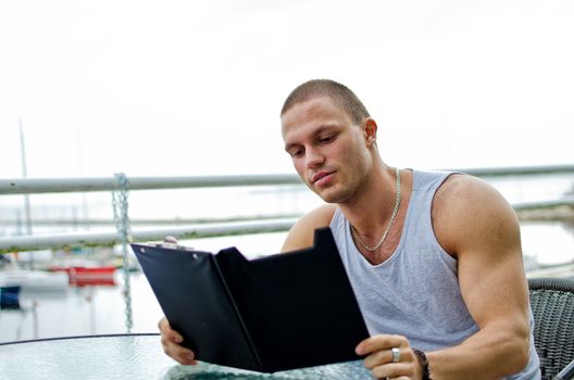 Handsome muscular male orders food in summer cafe.