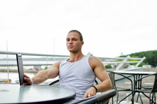 Handsome muscular male orders food in summer cafe.