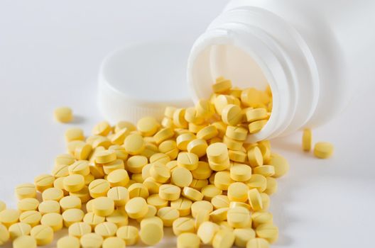 yellow pills out of white bottle on white background
