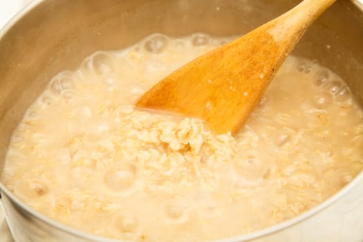 Healthy oatmeal cooking in a pot with a wooden spoon