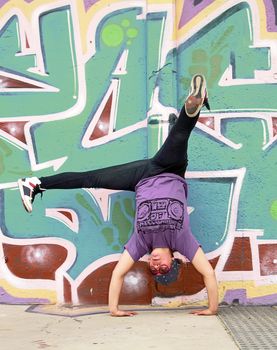 Hip-hop breakdancer handsatnding with a graffited wall as background