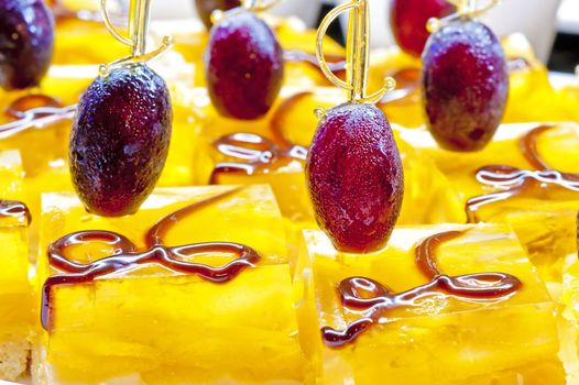 Dessert with fruit jelly and a grape on a stick.