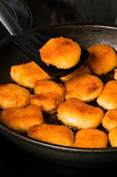 Fried nuggets in pan with one nugget on spatula