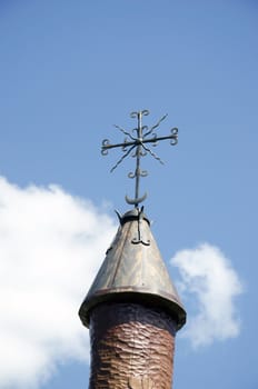 Sculpture carved from wood with roof and handmade steel decorations on background of cloudy sky.