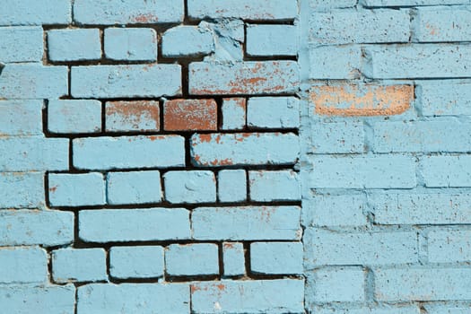 A blue pastel painted brick wall with signs of ware and an irregular pattern.